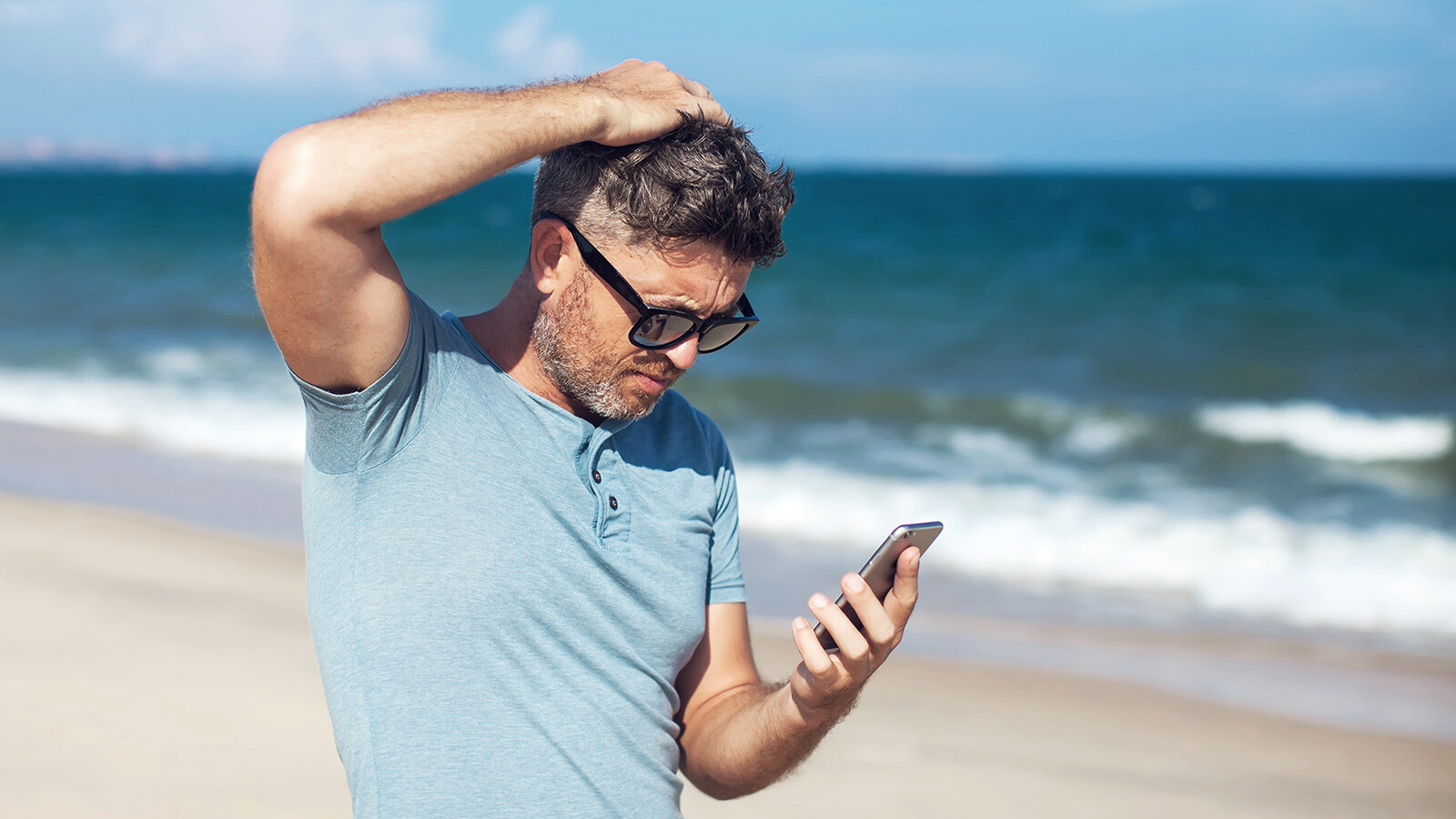 Man som är på stranden och tittar på sin mobil