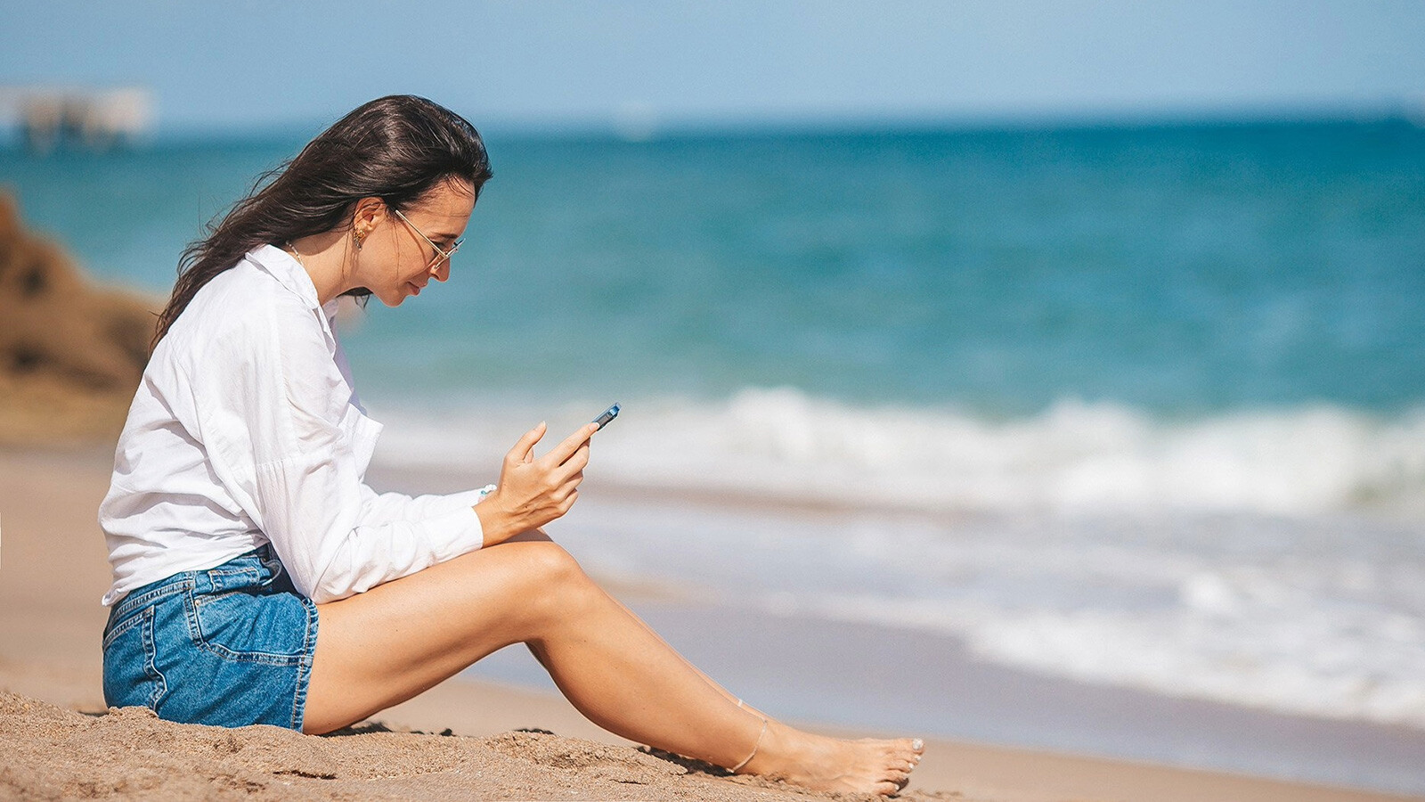 Dame som sitter på stranden med en telefon